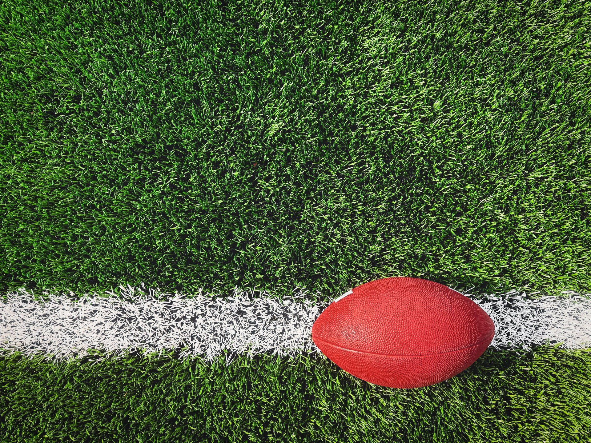 A minimalist overhead shot of an American football placed on a white yard line with clean synthetic turf