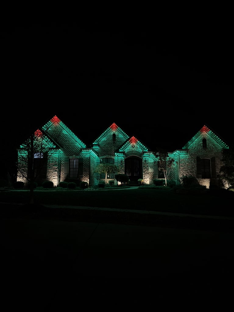 Stone house facade illuminated with green and red holiday lights at night against dark sky