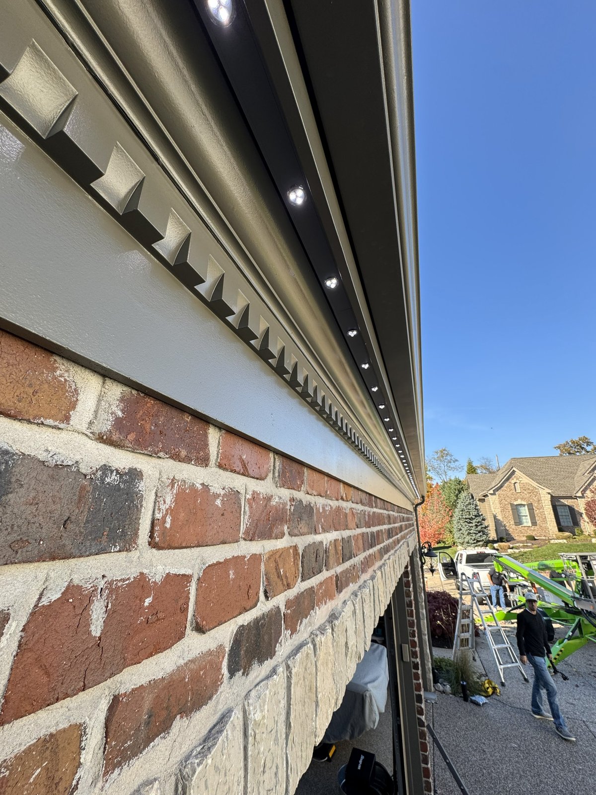 Modern soffit and fascia with LED lighting installed along brick building exterior against clear blue sky