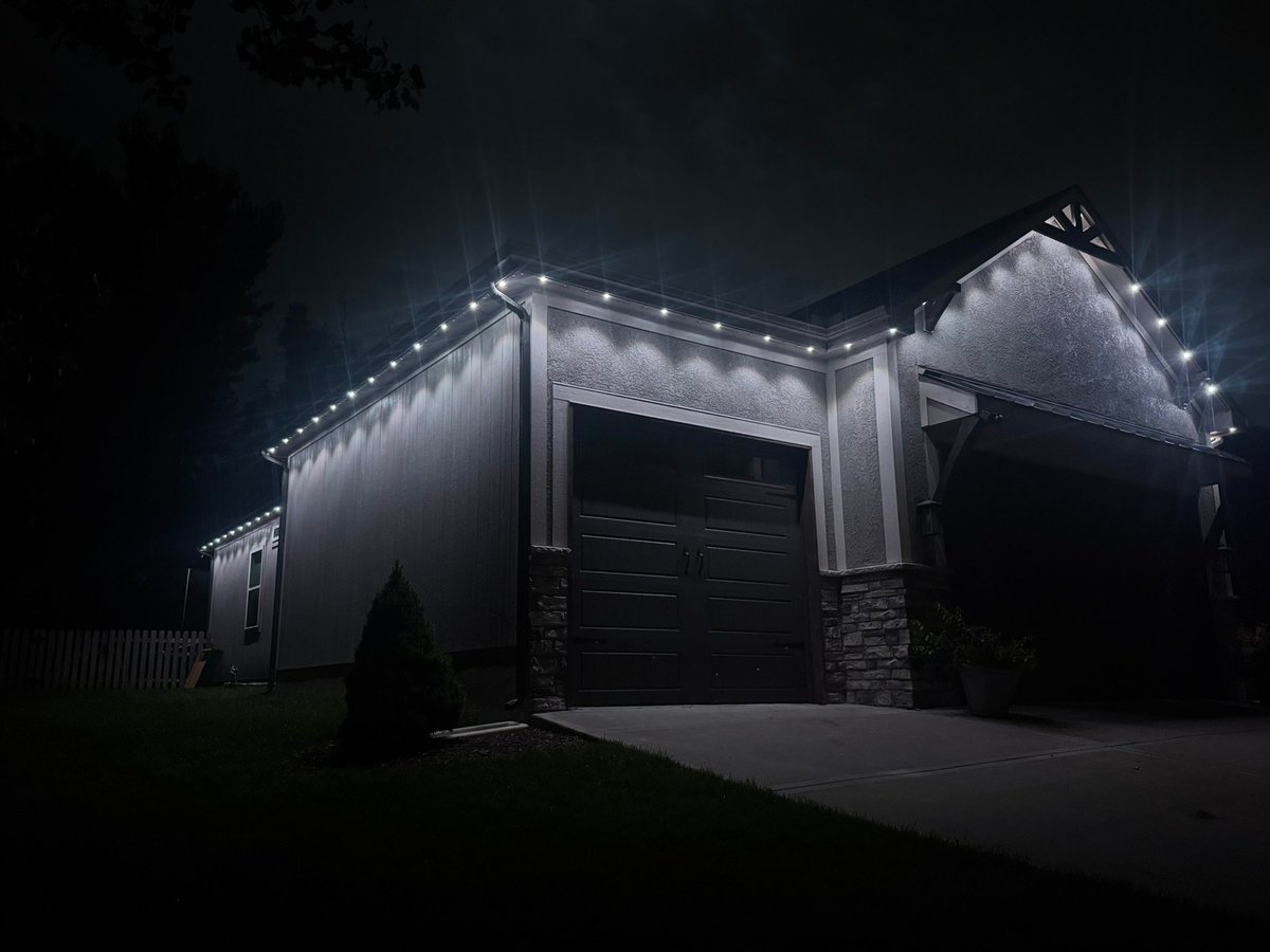 Modern garage with white LED trim lighting against dark night sky, featuring black garage door and stone accents.